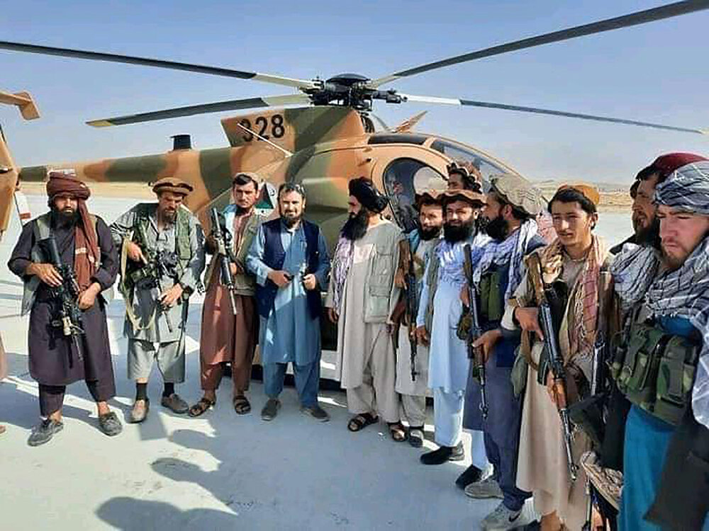 <p>Боевики позируют на фоне вертолета, захваченного у правительственных сил на авиабазе Мазари-Шариф, 15 августа 2021 года</p>