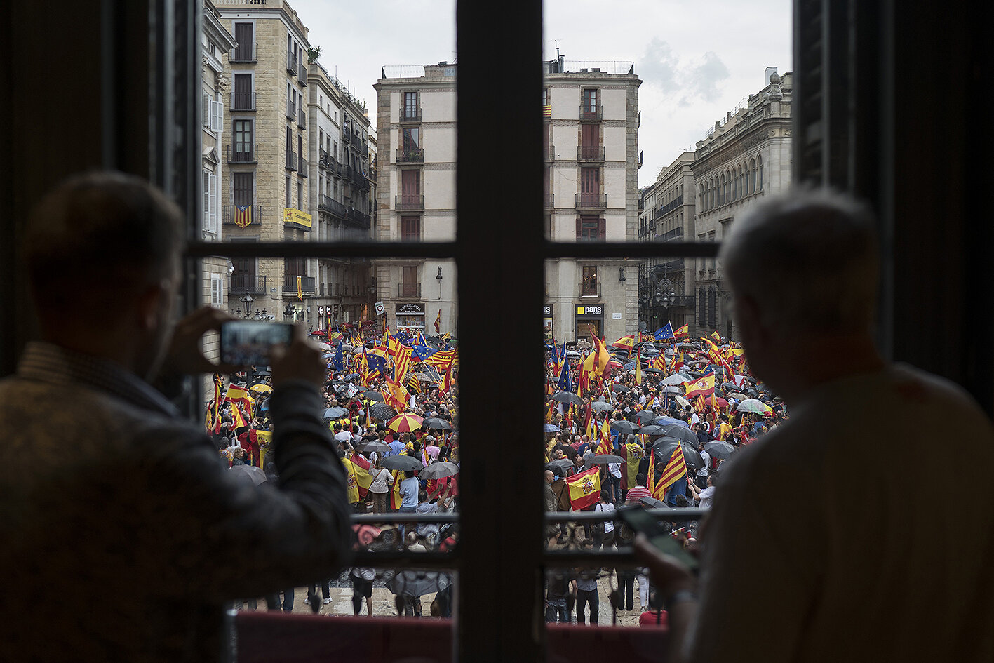 <p>Люди в кафе наблюдают за&nbsp;демонстрацией сторонников единства Испании, выступающих против отделения Каталонии.</p>