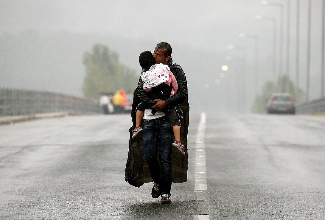 <p>Сирийский беженец с дочерью на руках направляется к границе Греции с Македонией. 10 сентября 2015 года</p>